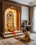 Woman praying in front of an ornate wooden deity shrine with floral decorations.