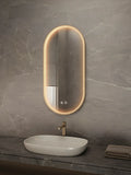 Bathroom vanity with a sink and illuminated oval mirror on a gray marble wall.